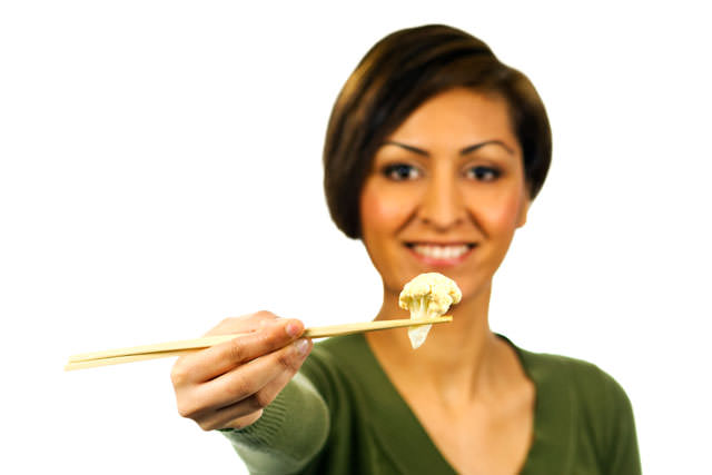 Young woman holds a piece of cauliflower with chopsticks