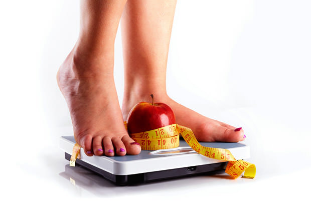 A pair of female feet standing on a bathroom scale with red appl