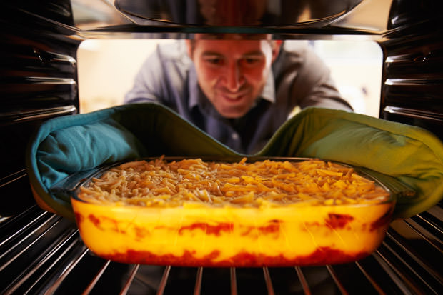 Man Putting Dish Of Lasagne Into Oven To Cook